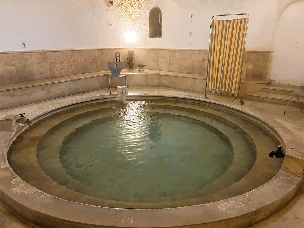 A tranquil circular bathing pool in a serene interior, featuring stone walls and soft lighting.