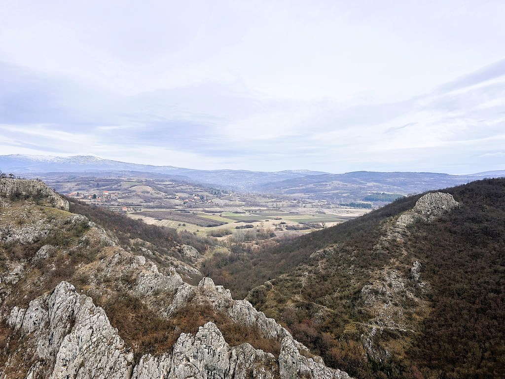 Scenic landscape view featuring rocky hills in the foreground and rolling valleys in the background under a cloudy sky.