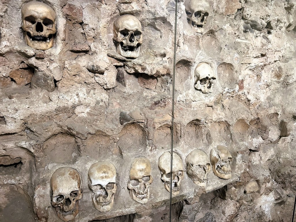 A wall displaying multiple human skulls embedded in a stone surface, showcasing a historical or archaeological context.