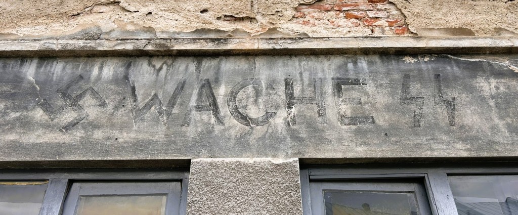 Faded inscription on a building wall featuring the text 'WACHE 44' alongside a swastika symbol.