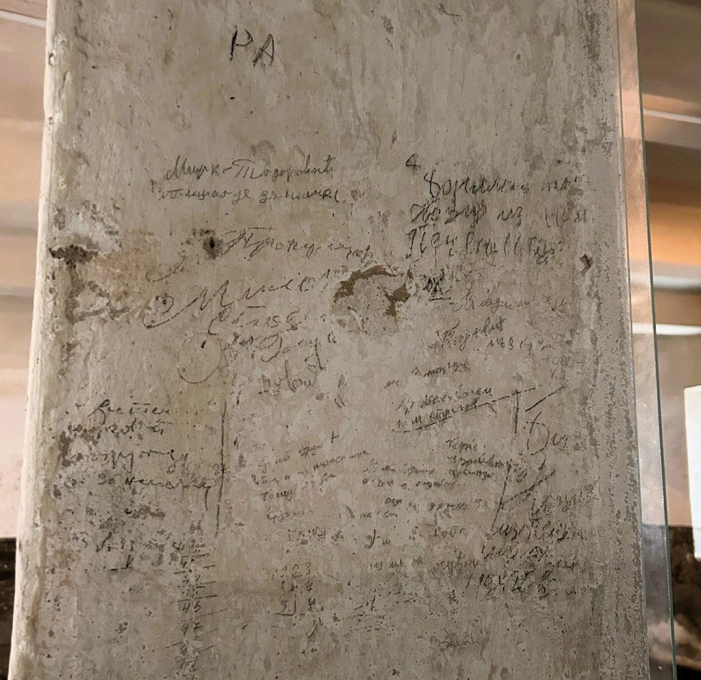 A close-up view of a textured wall featuring various inscriptions and scribbles, showcasing marks from different eras.