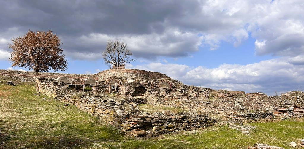 Ruins of an ancient structure made of stone with a backdrop of cloudy sky and sparse trees.