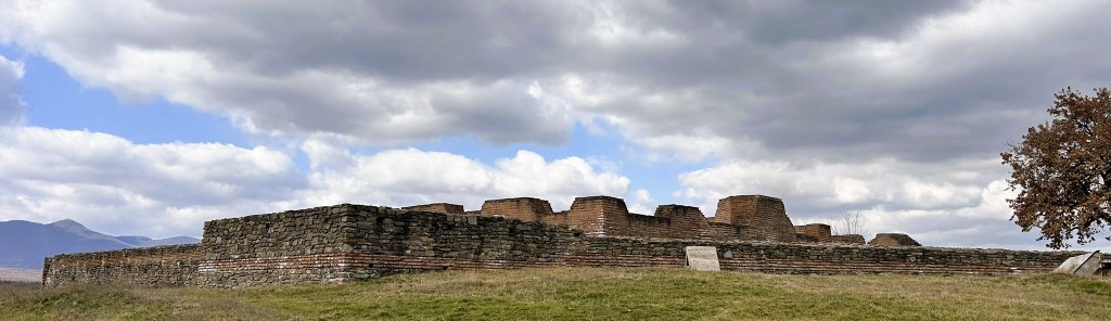 Ruins of an ancient stone structure set against a cloudy sky, with grassy surroundings.