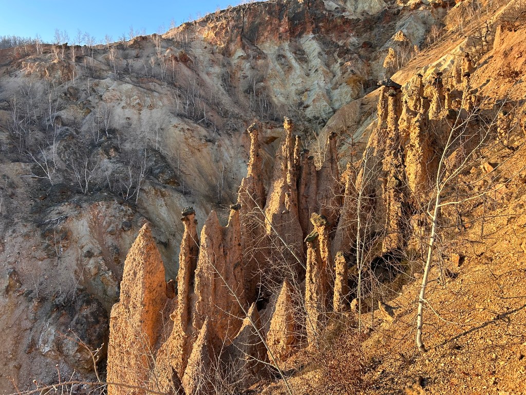 Tall, pointed rock formations with a steep, textured hillside in the background, showcasing a mix of earthy tones and sparse vegetation.