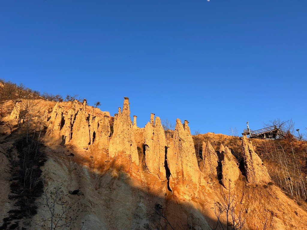 A rocky cliff with spire-like formations under a clear blue sky.