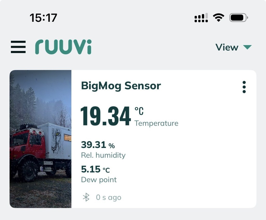 Digital display from a Ruuvi sensor showing temperature, relative humidity, and dew point, with a BigMog vehicle in the background.