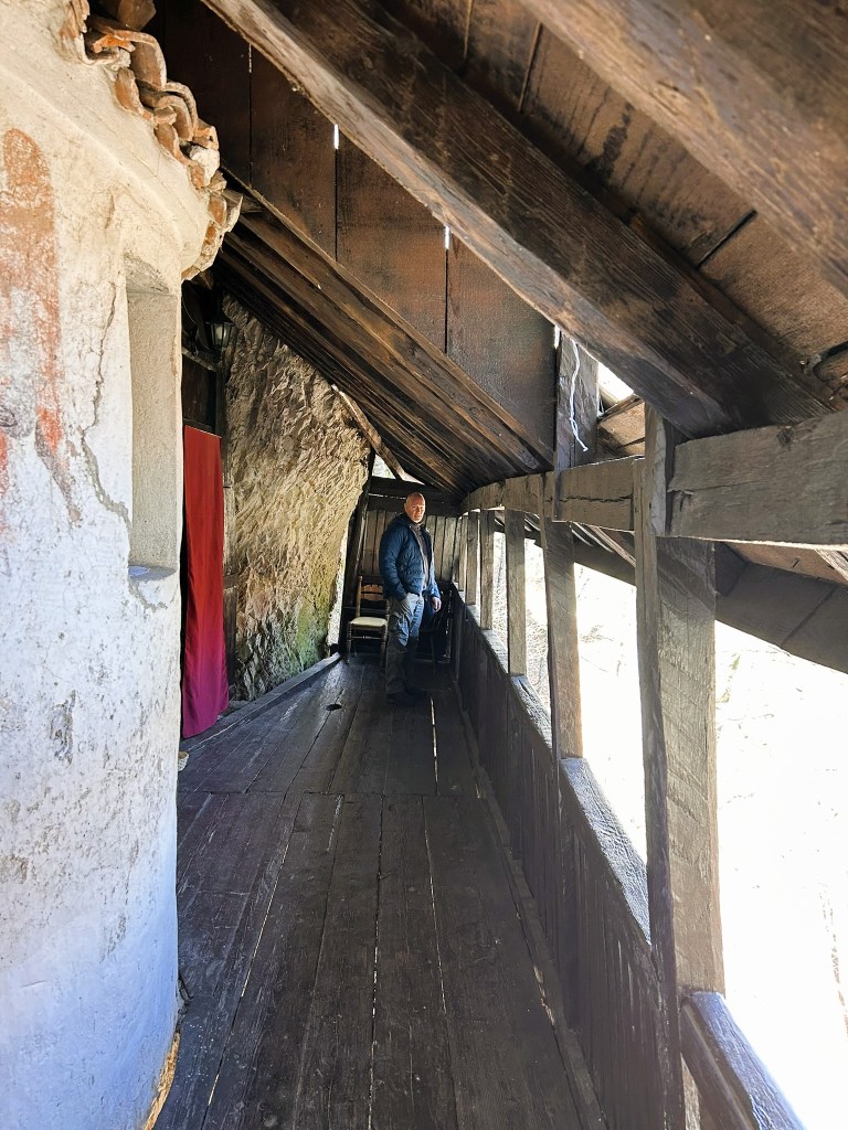 A person standing on a wooden walkway inside a rustic building with stone walls and a sloped roof.