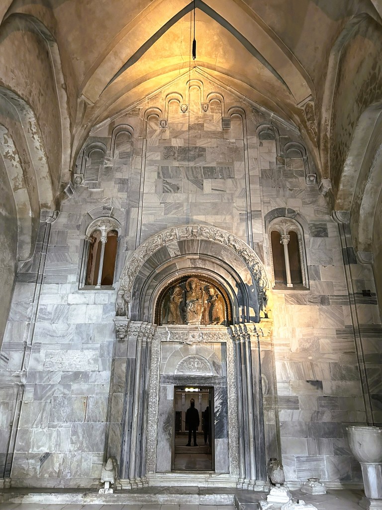 Interior view of a stone church entrance with intricate carvings and a large archway, featuring a figure silhouetted in the doorway.