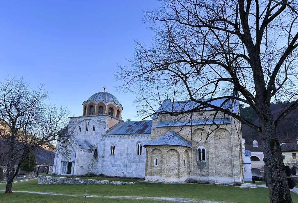 A historic stone church with a dome, surrounded by leafless trees and a clear blue sky.