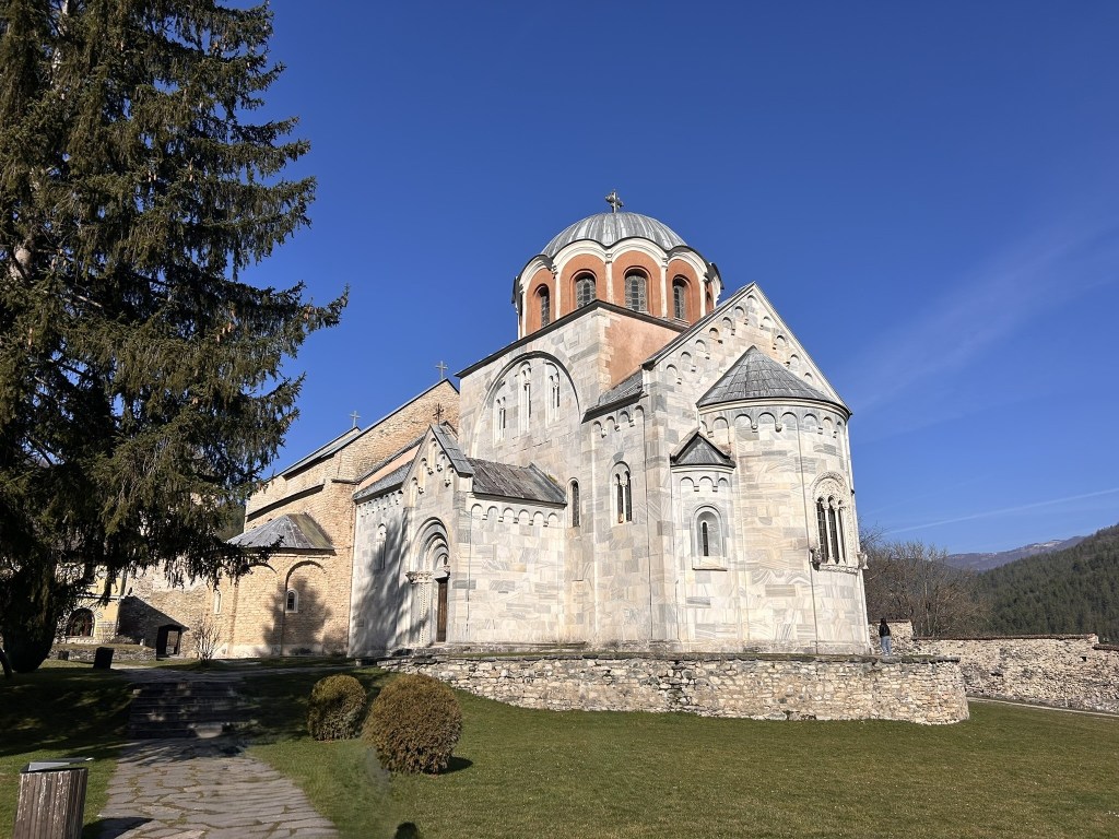 A stone church with a domed roof, set against a clear blue sky and surrounded by greenery.