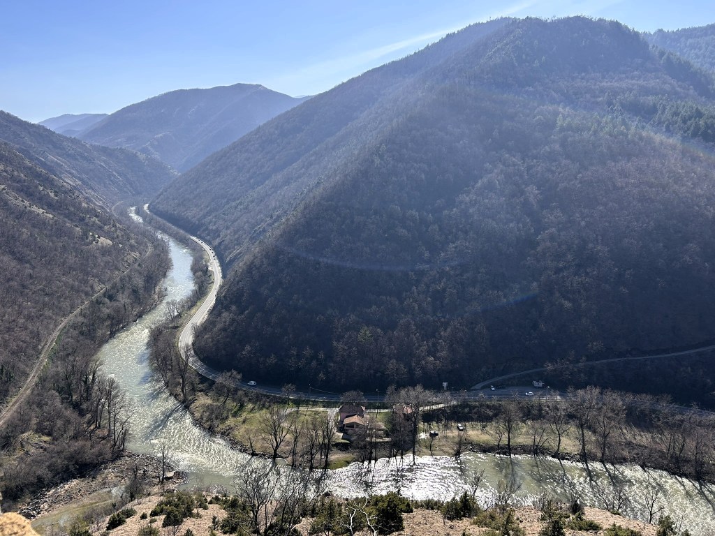 A panoramic view of a winding river surrounded by steep, forested hills under a clear blue sky.