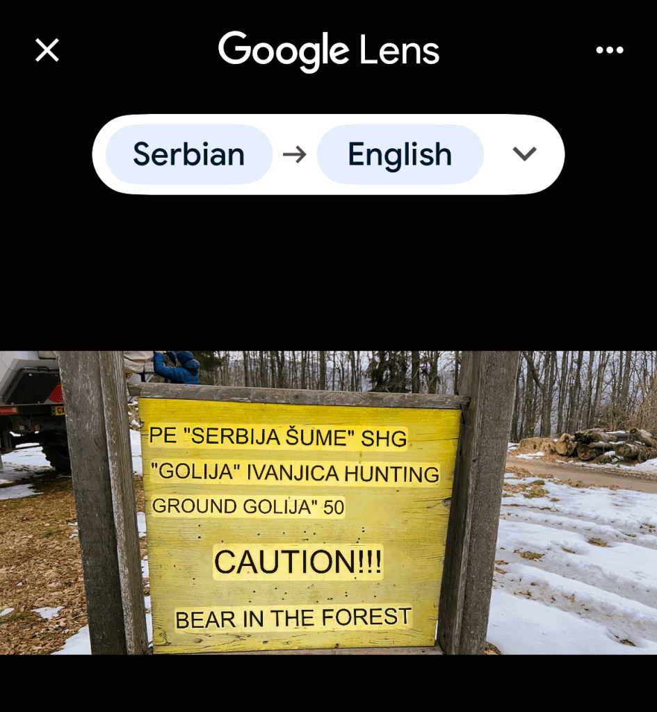 A wooden sign warning of a bear in the forest, located near a snowy area, with text in Serbian about hunting grounds and caution.
