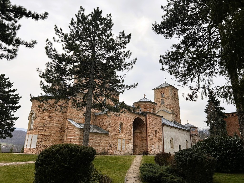 Historic brick church surrounded by trees and greenery, set against a cloudy sky.