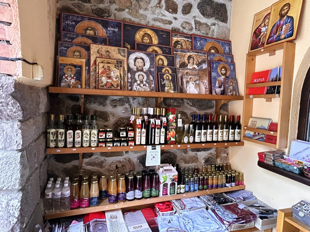 A wooden shelf displaying various religious icons and paintings, alongside bottles of traditional drinks and other local products.