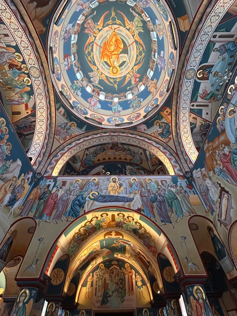 Interior view of an ornate church featuring intricate frescoes on the domed ceilings and walls, depicting various saints and biblical scenes.