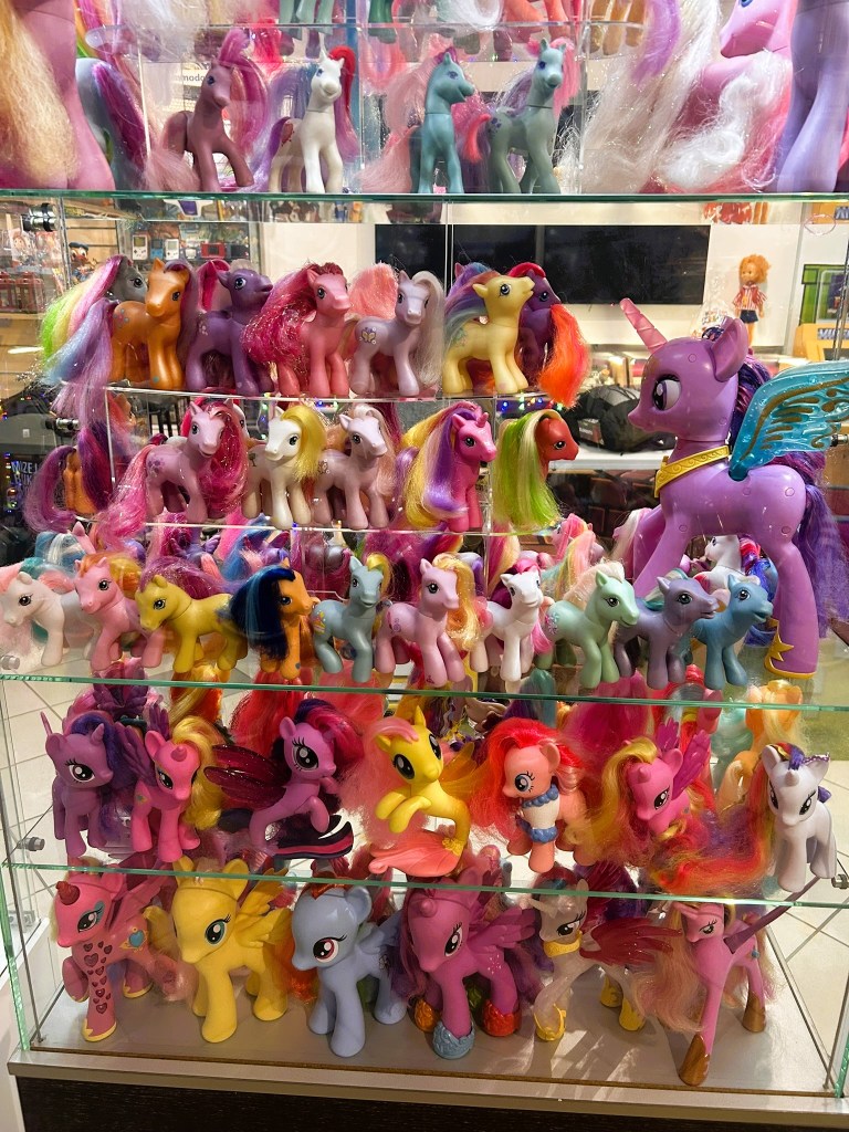 A display case filled with various colourful toy ponies, showcasing different characters from the My Little Pony franchise, arranged in multiple rows.