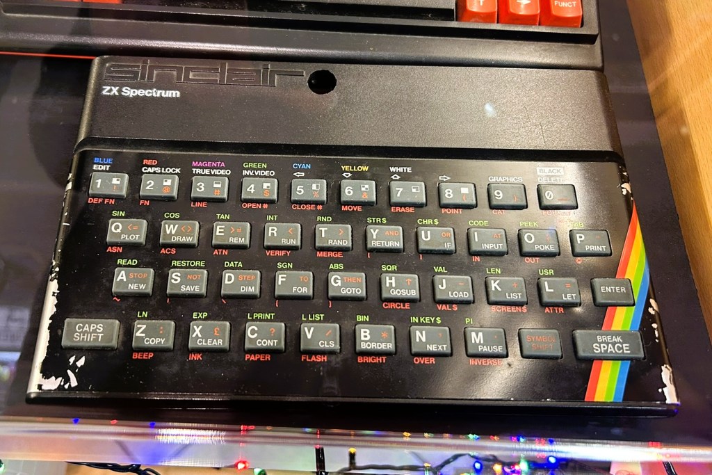 Close-up of a ZX Spectrum keyboard, showcasing a range of colourful keys and labels, including function keys and control buttons, with visible wear on some edges.