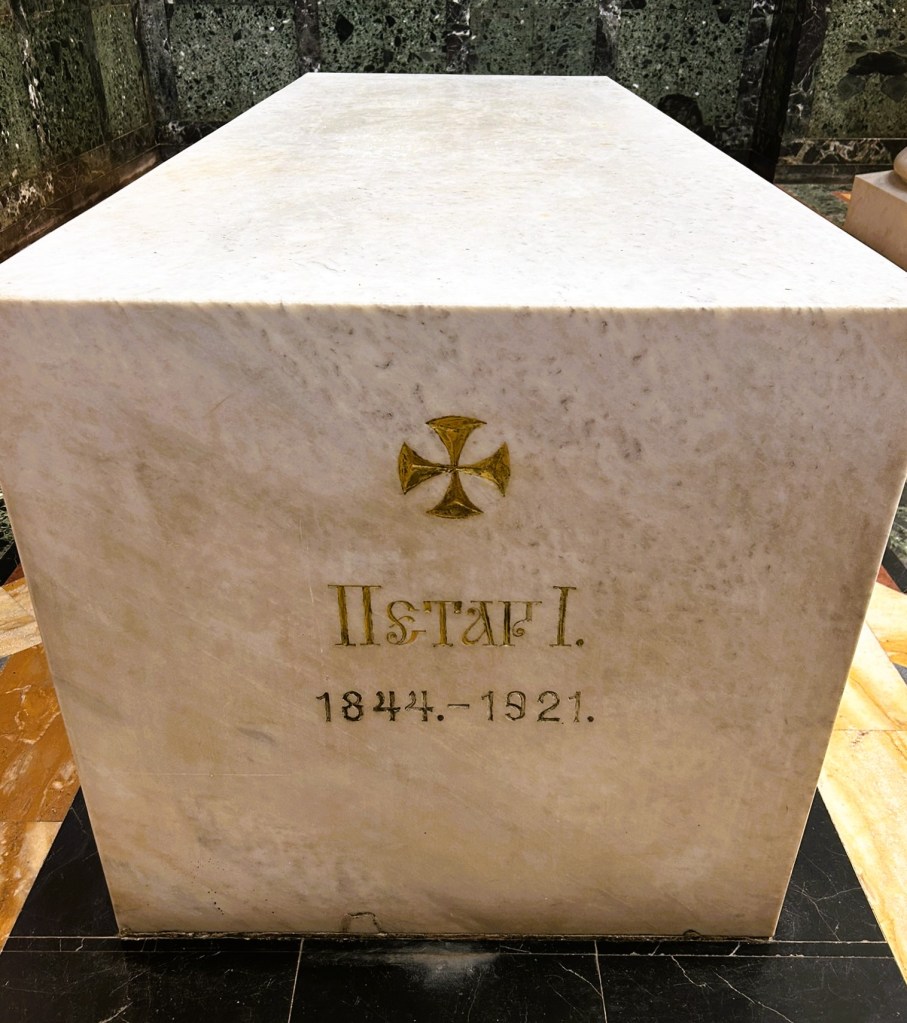 A marble tombstone inscribed with 'Пётр I. 1844-1921' and a golden cross symbol.