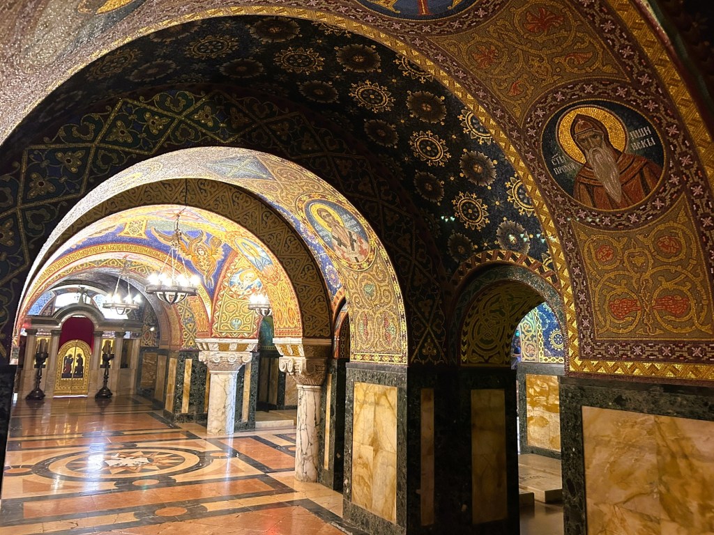 Interior view of a beautifully adorned corridor with mosaic ceilings and intricate patterns, featuring arches and ornate decoration.