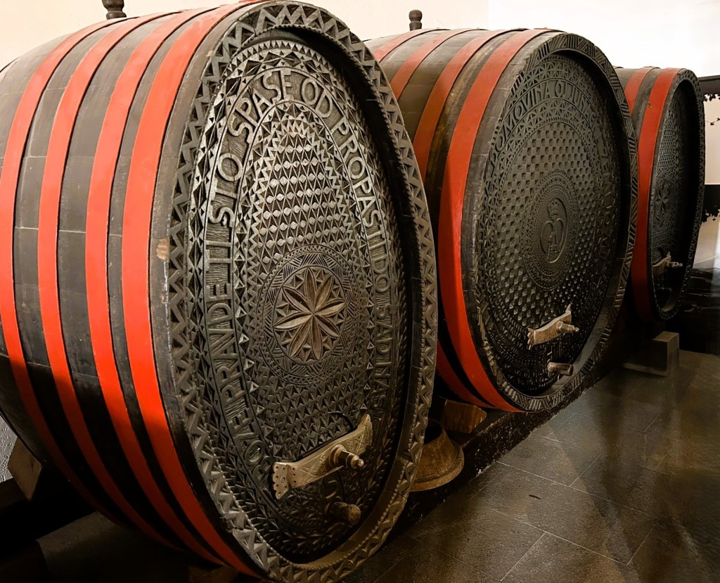 Three large, intricately designed wooden barrels with red and black stripes, featuring embossed patterns and metal spigots.