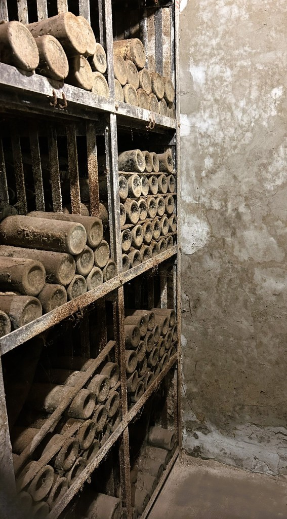 A dusty storage room featuring metal shelves filled with cylindrical objects, stacked neatly and showing signs of age and neglect.