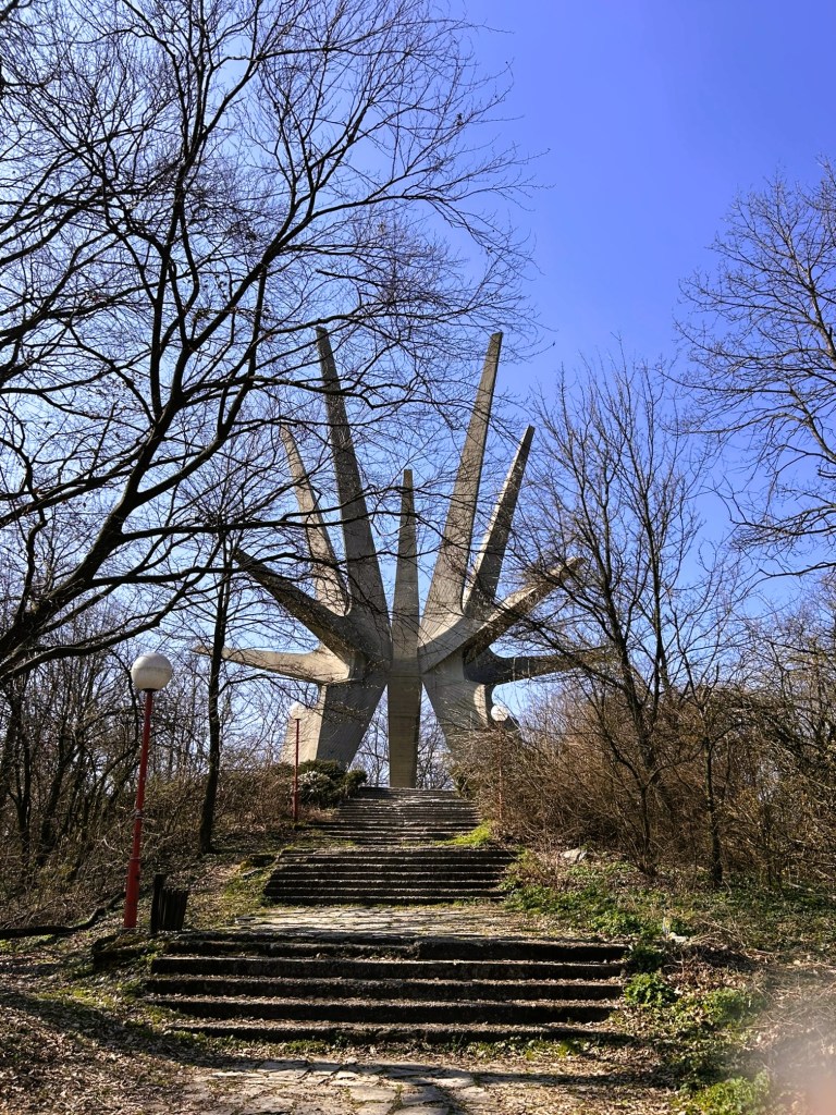 A large concrete monument resembling a star, surrounded by bare trees and a clear blue sky, with stone stairs leading up to it.
