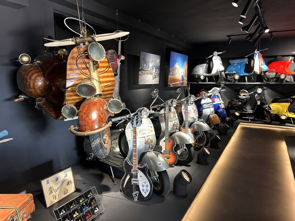 A display of vintage scooters and unique vehicles, including a wooden scooter with distinctive features and several classic models in a dark-toned interior.
