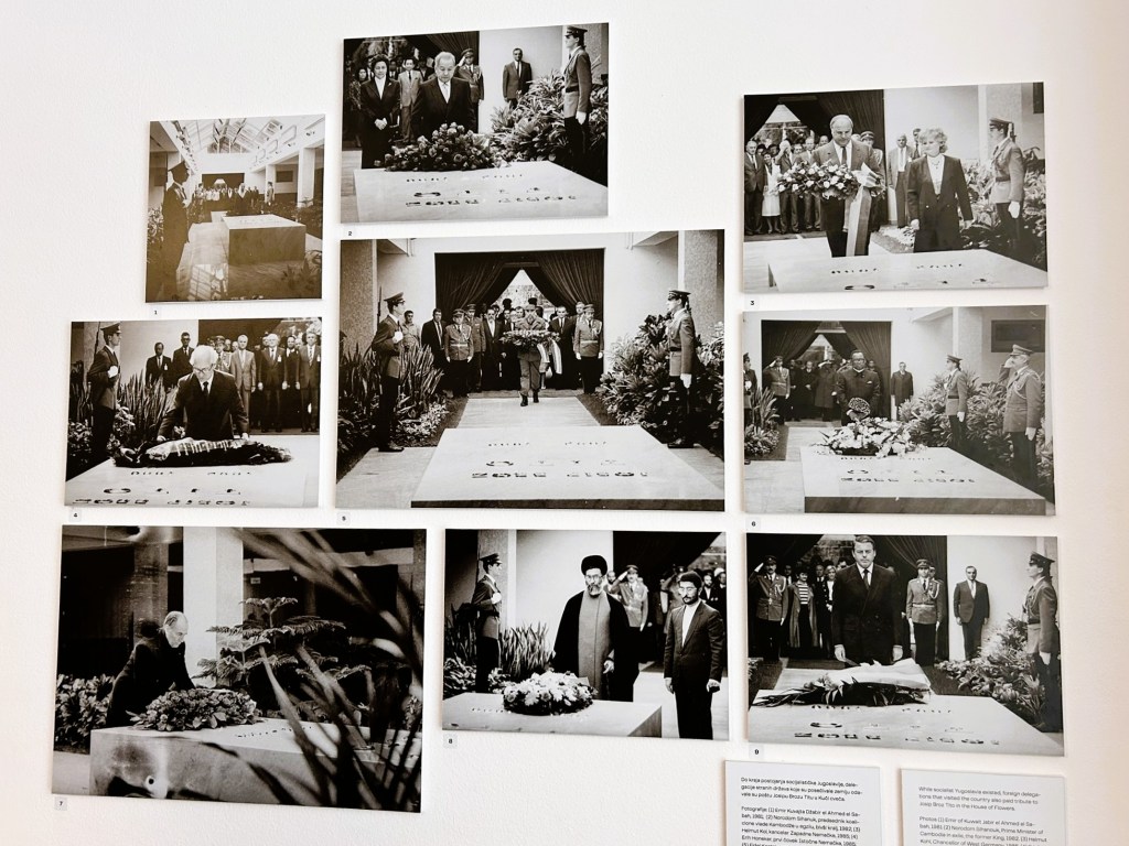 A collage of black and white photographs displayed on a wall, depicting various dignitaries and officials at a memorial site with floral tributes.