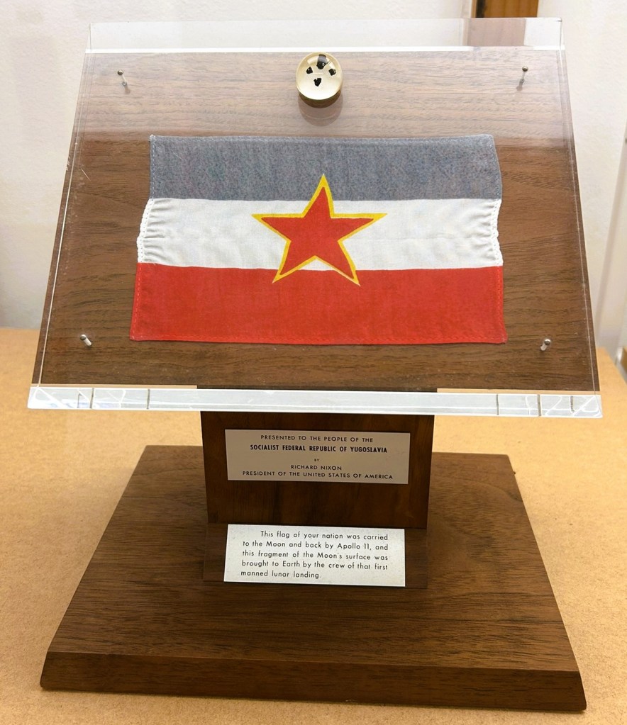 Display case containing a flag of the Socialist Federal Republic of Yugoslavia, presented by President Richard Nixon, with an inscription detailing its journey to the Moon and back by Apollo 11.
