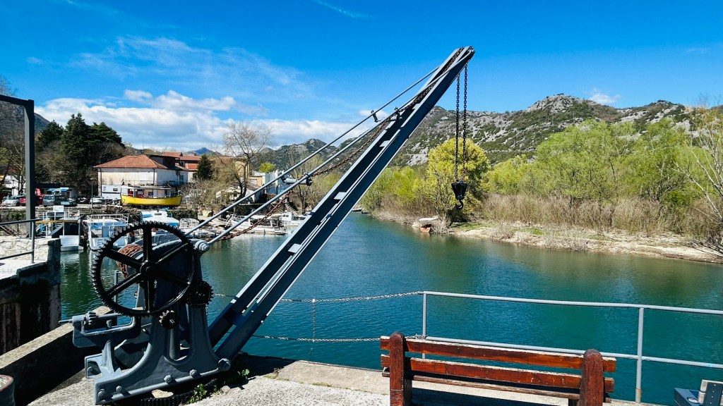 A historical crane beside a river, with a clear blue sky and greenery in the background.