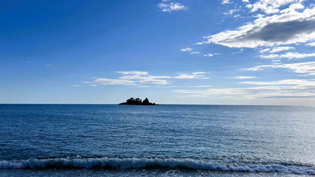 A serene seascape featuring a calm blue ocean under a clear sky with scattered clouds, and a small island visible in the distance.