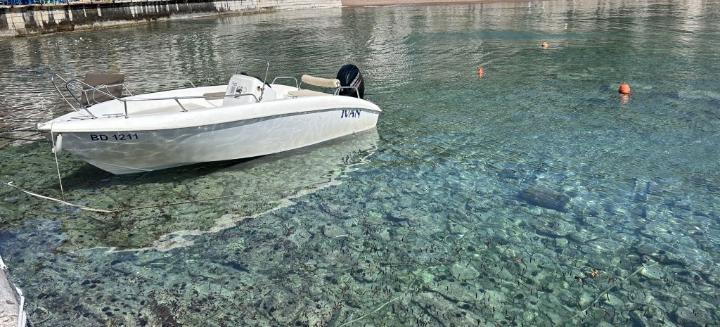 A small white boat docked in clear water, showcasing the rocky seabed beneath it.