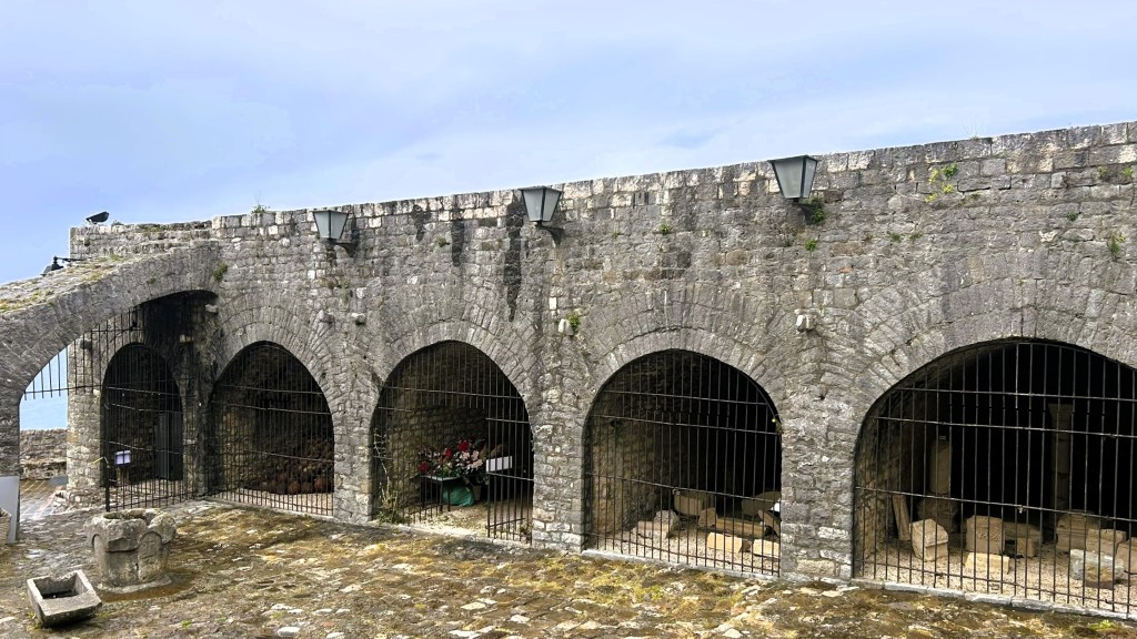 Exterior view of a stone structure with arches and metal grilles, featuring lanterns and a stone pathway.