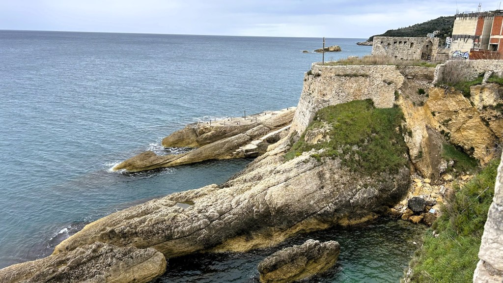 Scenic view of rocky cliffs leading to the sea, with an old coastal fortification in the background.