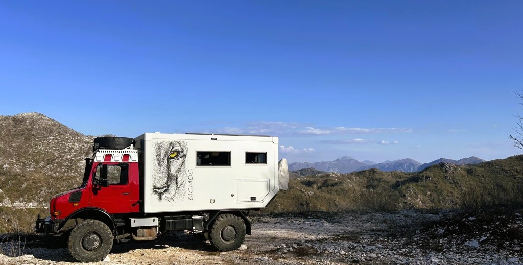 A rugged off-road vehicle parked on a mountainous terrain under a clear blue sky, featuring a unique lion graphic on its side.