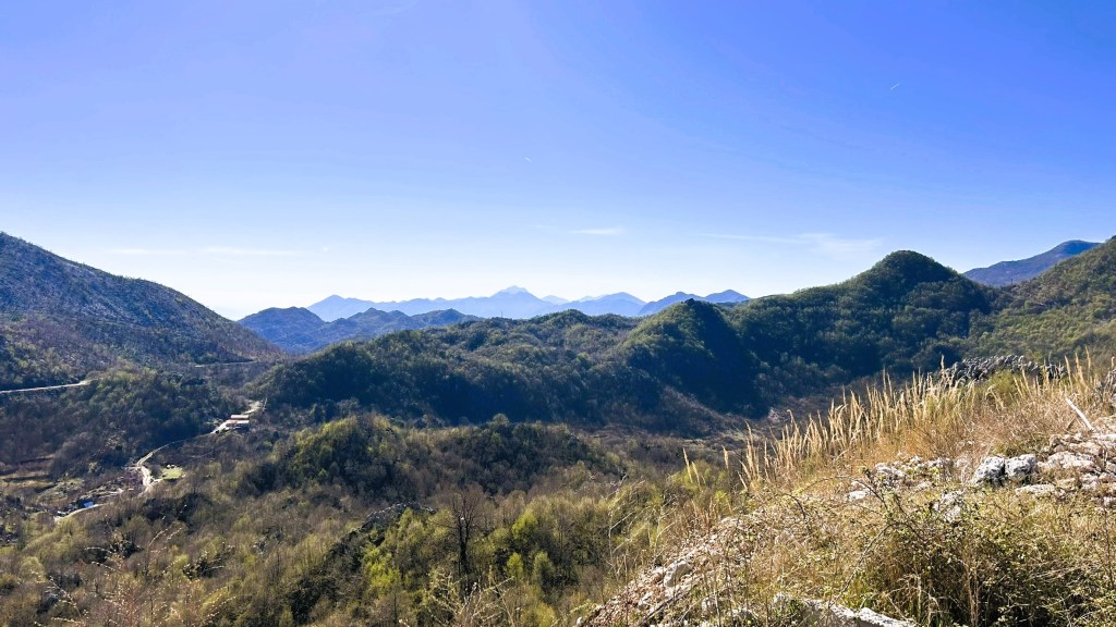 A panoramic view of rolling green hills and mountains under a clear blue sky.