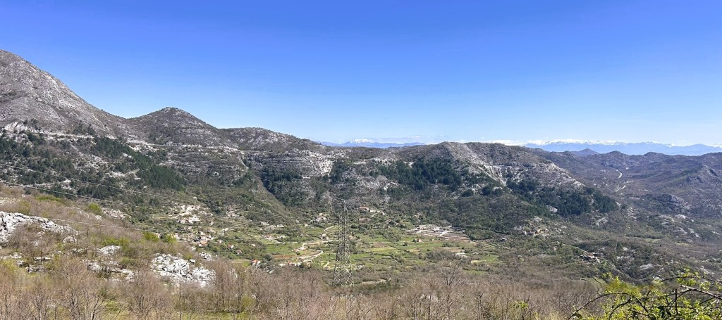 A panoramic view of rolling hills and mountains under a clear blue sky, showcasing a rural landscape with scattered villages and farmland.