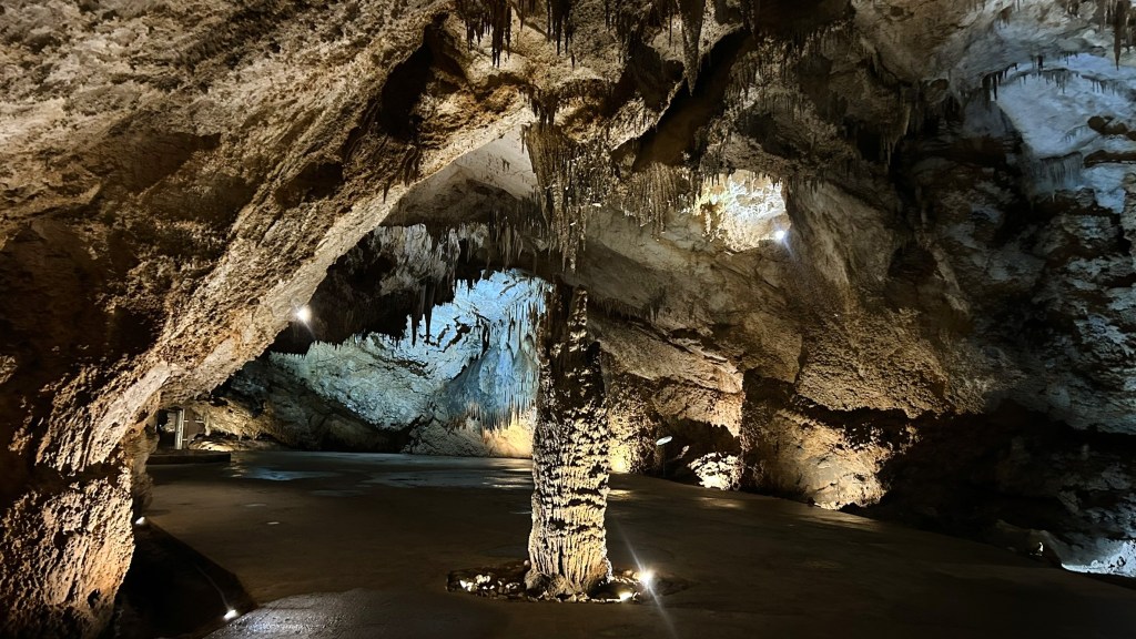 A large underground cave with stalactites and stalagmites, featuring an illuminated rocky structure and smooth floor.