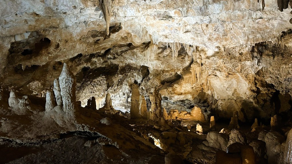 Interior of a cave featuring stalagmites and stalactites with illuminated sections.