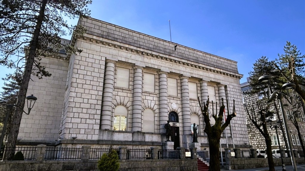 A grand historic building featuring classical architecture with tall columns and decorative stonework, set against a clear blue sky.