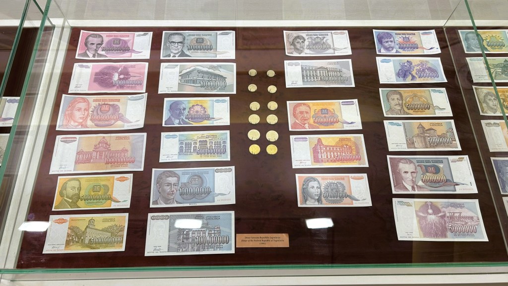 A display case featuring various banknotes and coins from a currency collection, arranged in rows with notable figures and landmarks depicted on the notes.