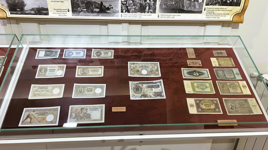A display case containing various banknotes arranged on a red background, showcasing historical currency from different periods.