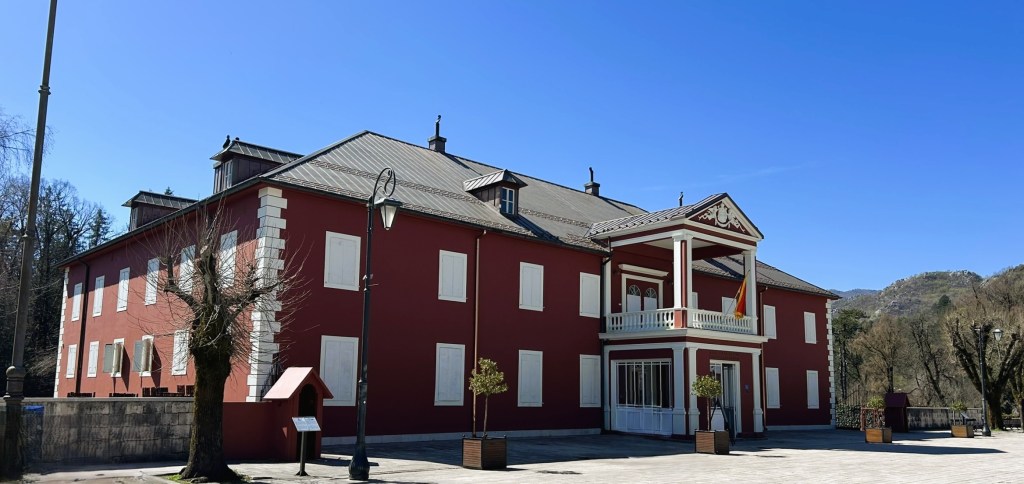 A large red building with white windows and a decorative balcony, set against a clear blue sky.