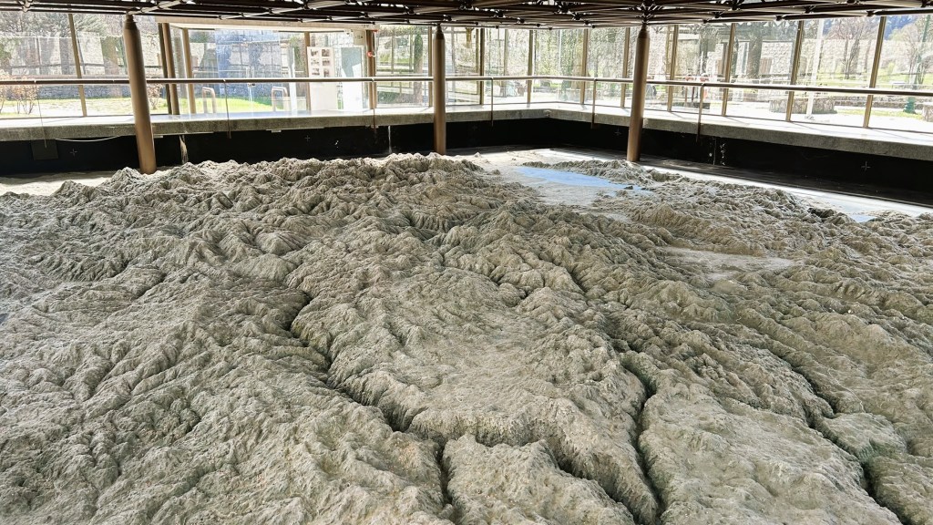 A large, textured topographical model resembling mountains, displayed indoors with natural light illuminating the features.