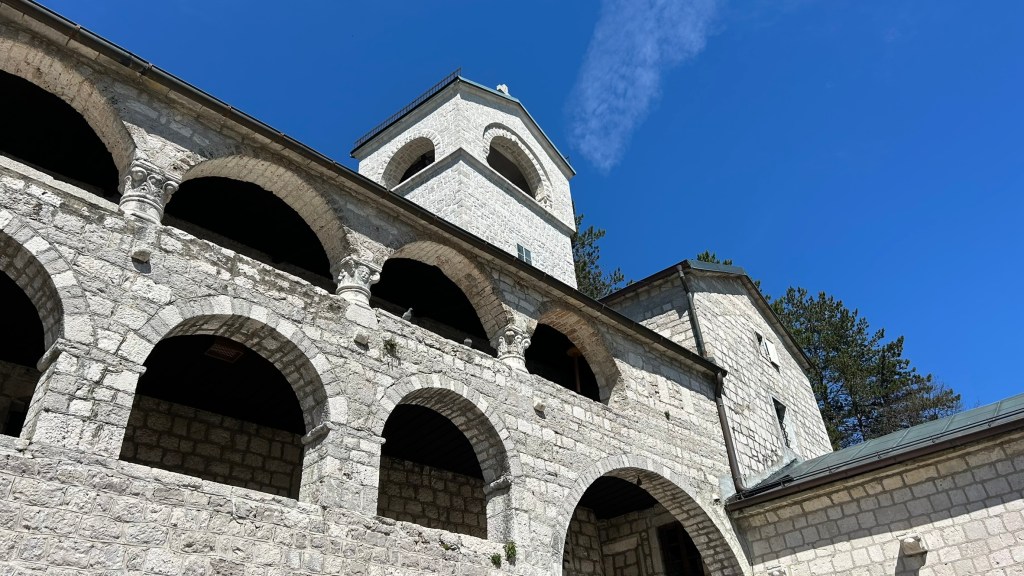A view of a stone building featuring arched walkways and a bell tower against a clear blue sky.