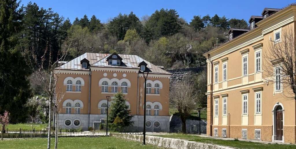 Two historical buildings set against a backdrop of green trees under a clear blue sky.