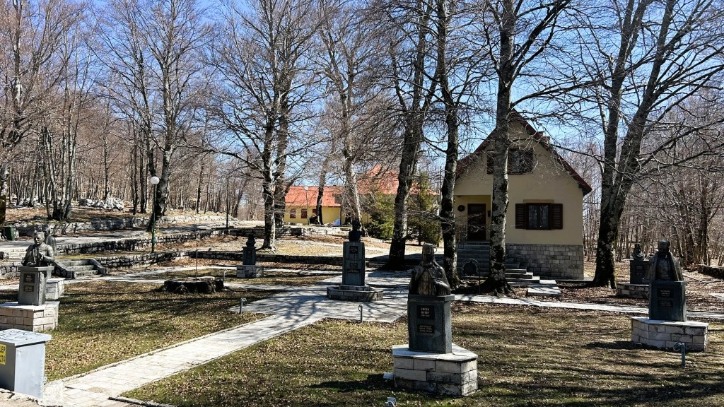 A peaceful outdoor area featuring several statues, bare trees, and a quaint house with a red roof in the background.