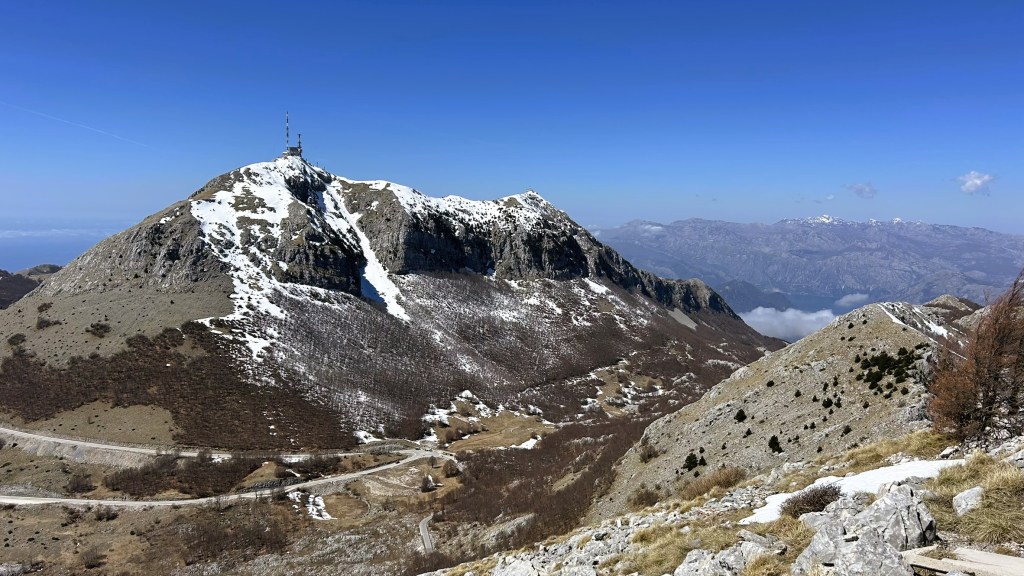 A panoramic view of snow-capped mountains under a clear blue sky, highlighting a peak with a communications tower at the summit.