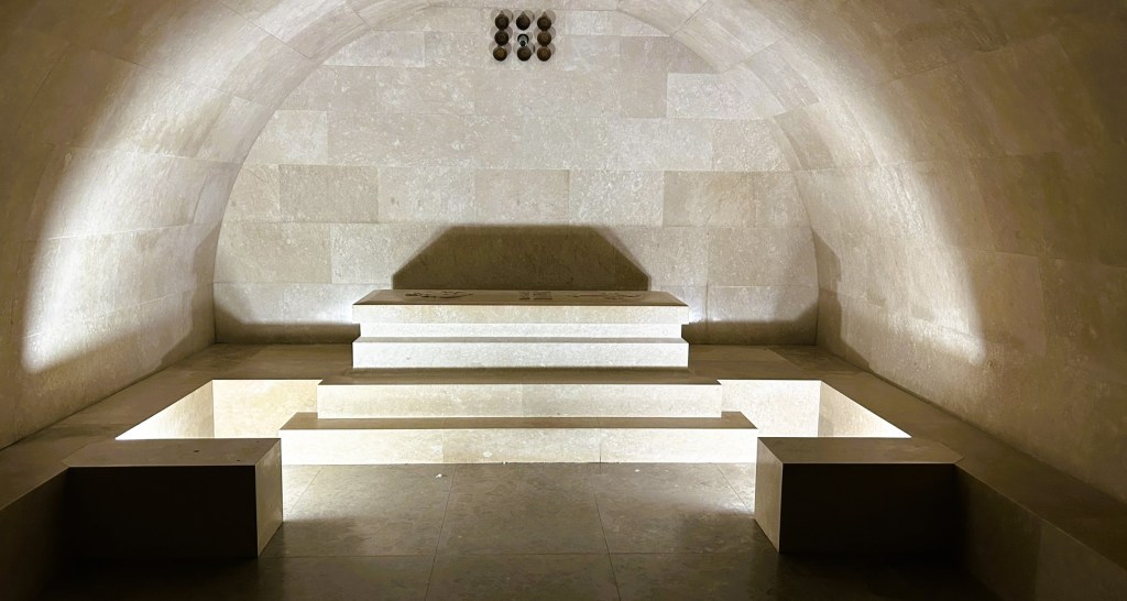 An elegantly designed dimly lit room with curved stone walls and illuminated steps, creating a serene and tranquil atmosphere.
