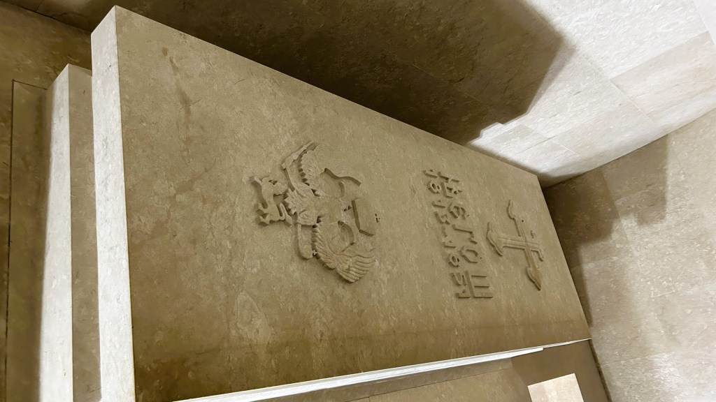 Close-up of a stone slab featuring an emblem and inscriptions, set in a minimalist interior.